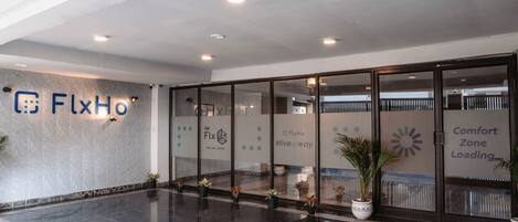 A modern hotel lobby with a polished floor, glass doors, and potted plants.