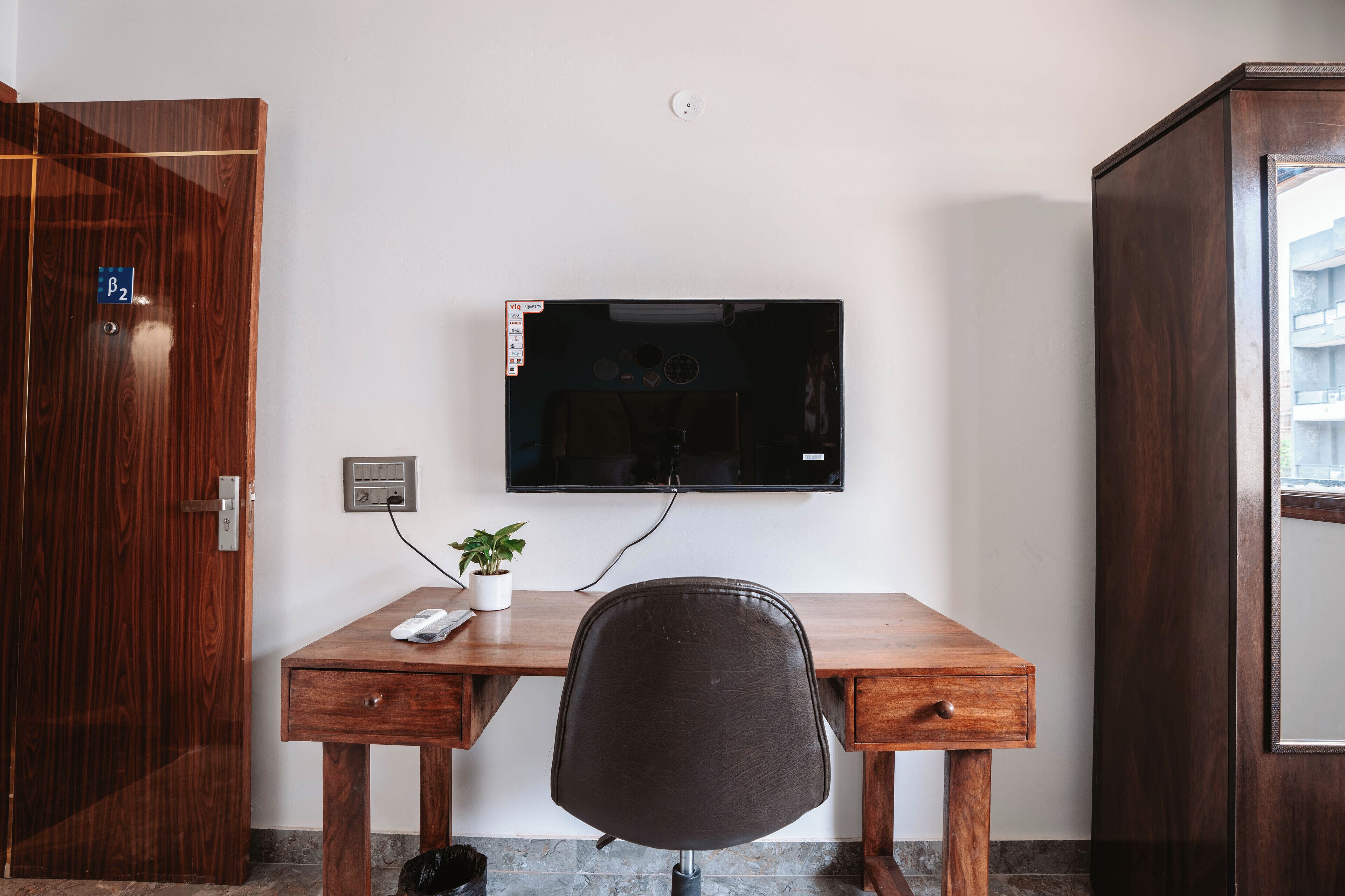 Un bureau en bois avec un téléviseur fixé au mur, une plante en pot et une chaise.
