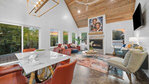 A spacious living room with a fireplace, large windows, and a ceiling fan.