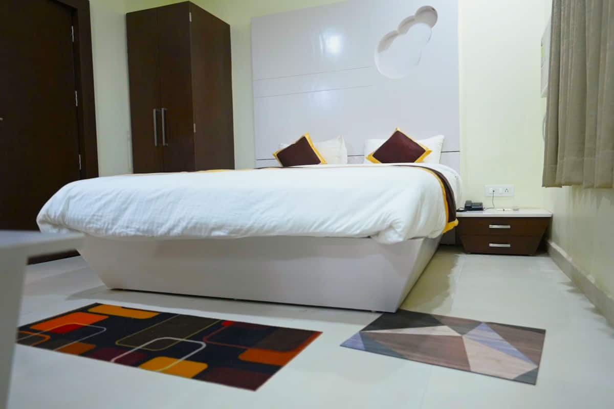 A bedroom with a large bed, a wardrobe, a nightstand, and a patterned rug.