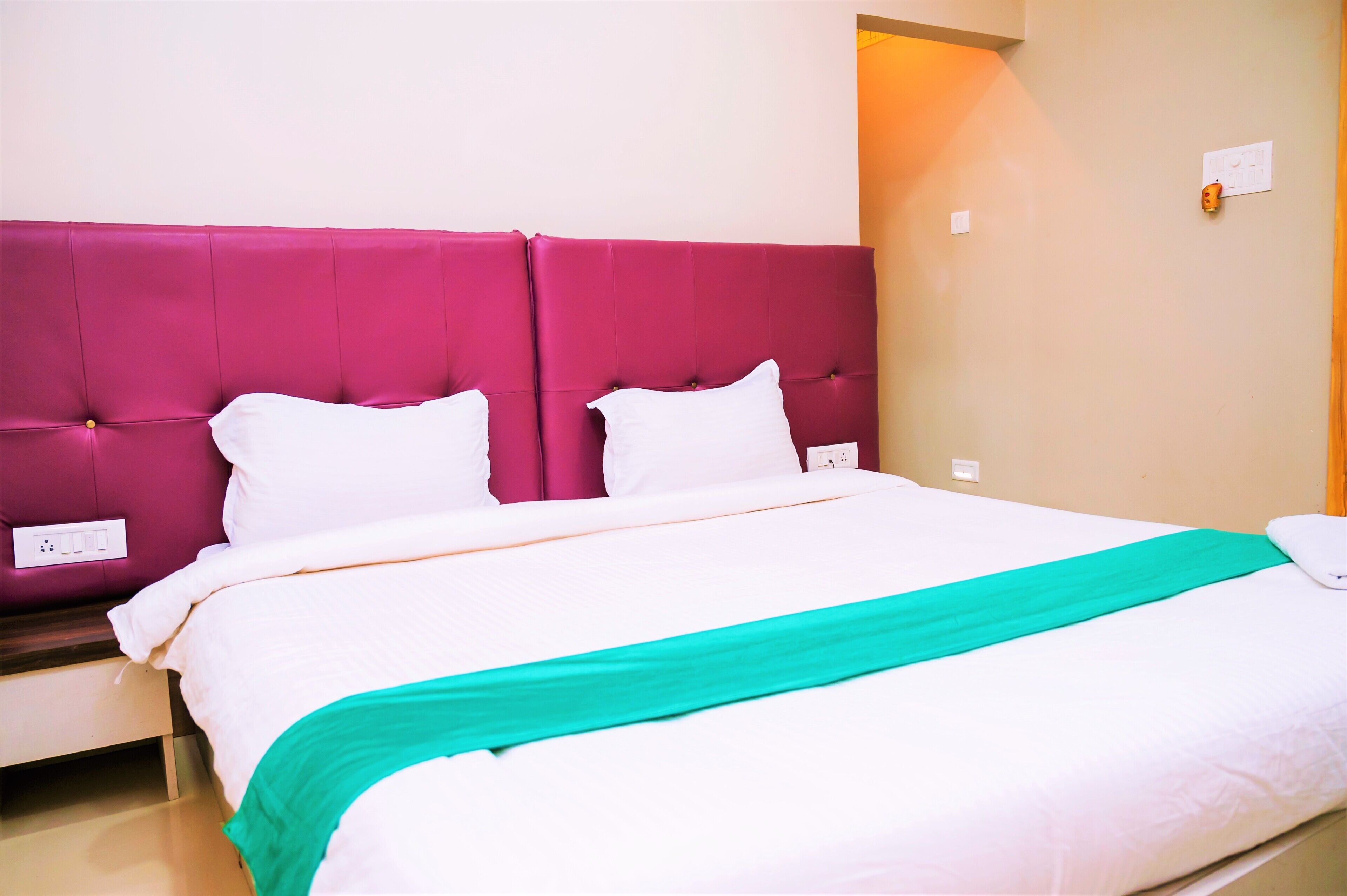 A bed with a white and teal bedspread, a pink headboard, and white pillows.