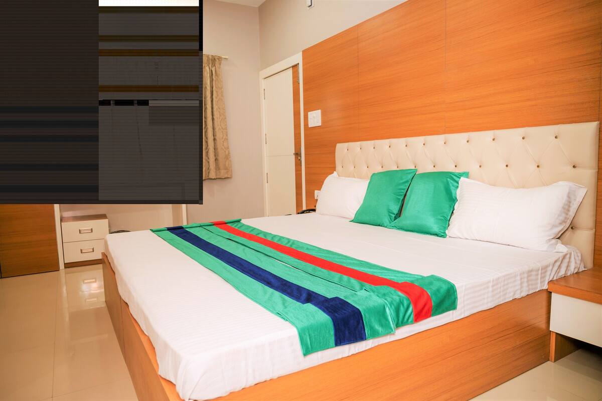 A hotel room with a large bed, wooden headboard, white bedding, and a striped throw blanket.