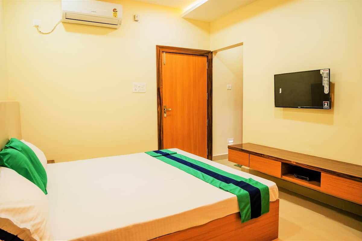 A hotel room with a bed, a wooden nightstand, a television, and an air conditioning unit.