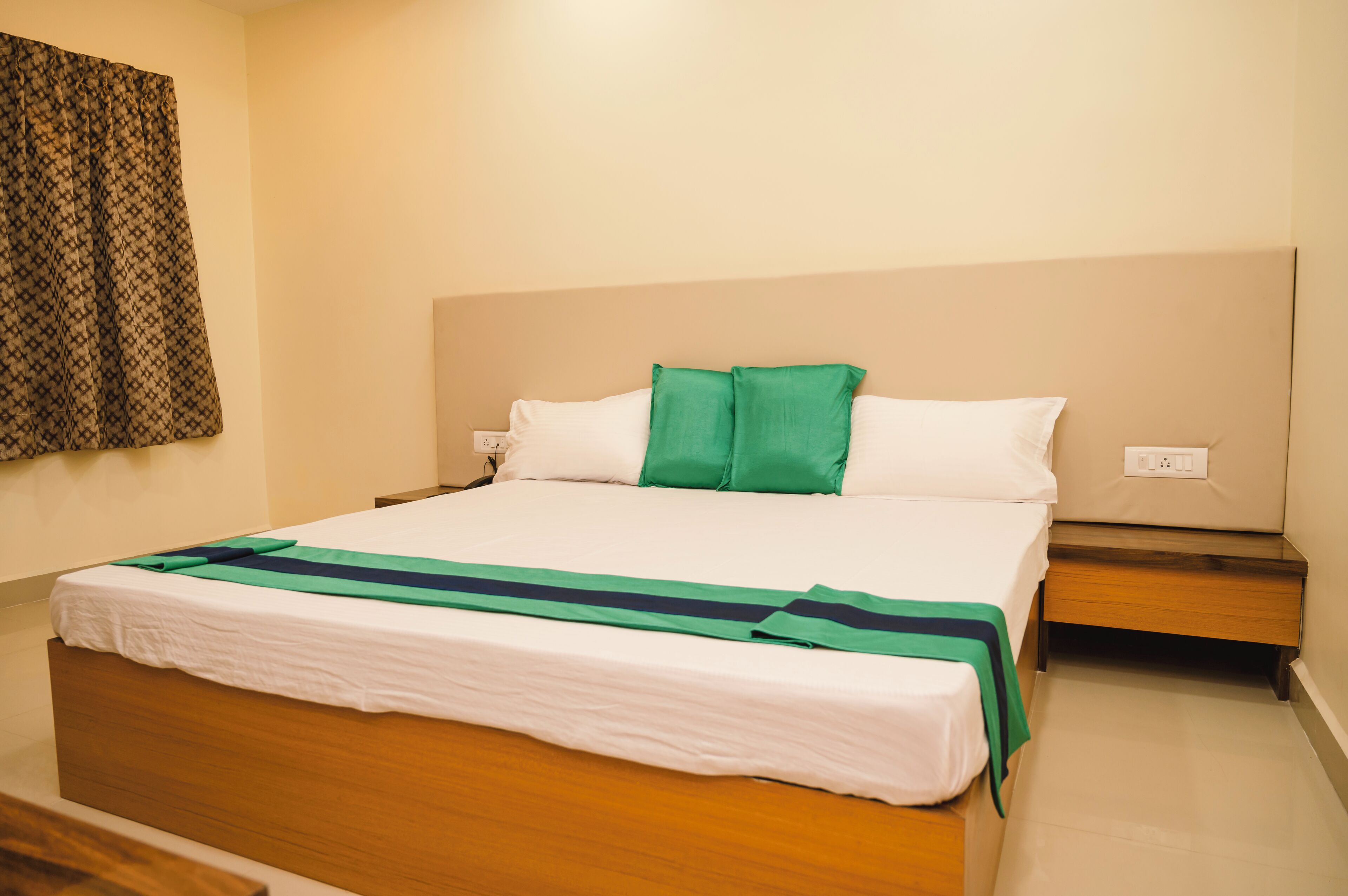 A neatly made bed with white and green bedding, a wooden headboard, and a bedside table with a lamp.