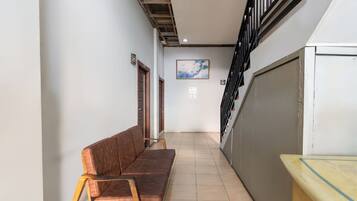 A narrow hallway with a brown sofa, a wooden bench, and a staircase with a black railing.