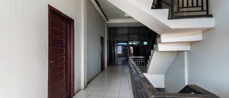 A hallway with a red door, a staircase with black railings, and a tiled floor.