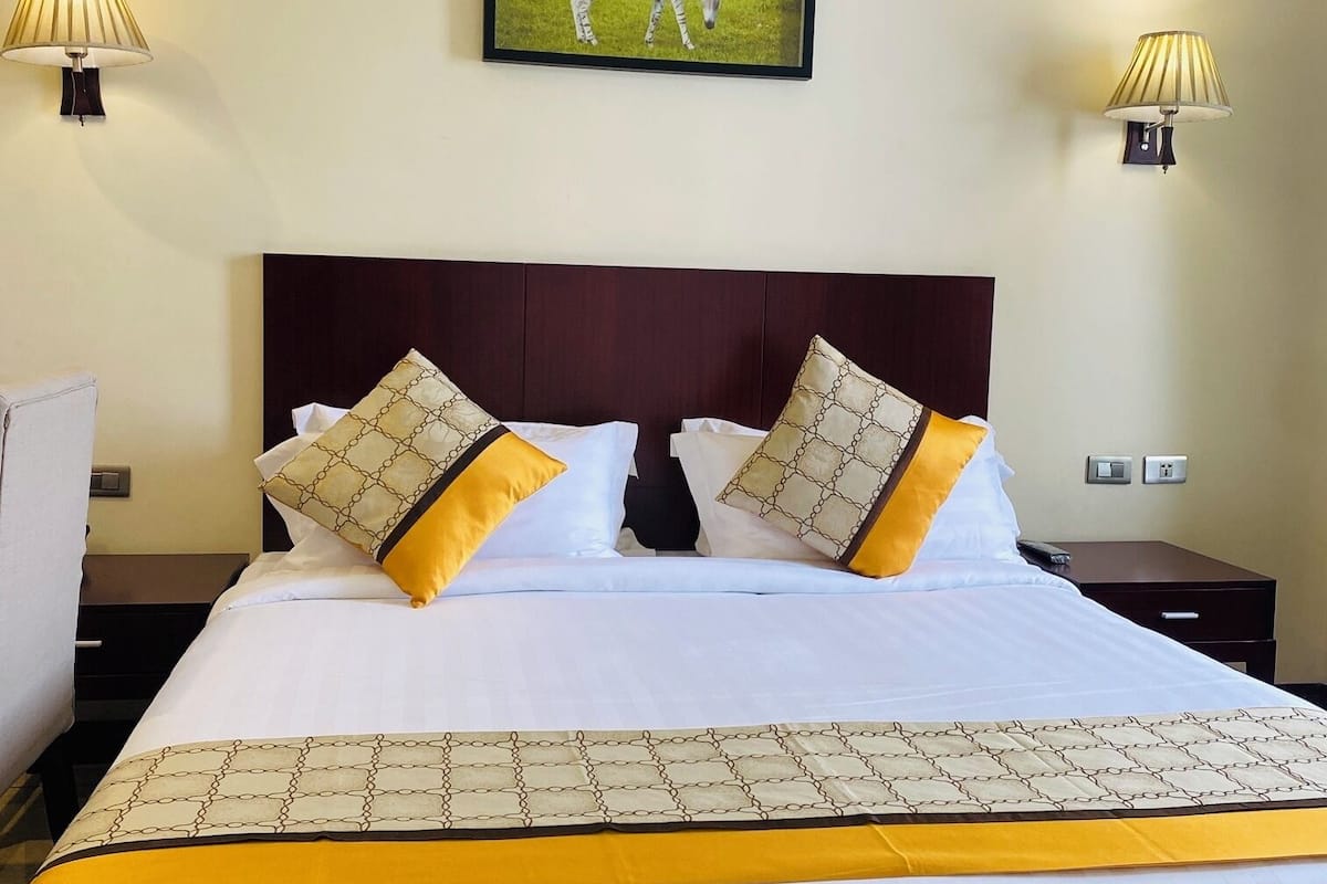 Une chambre d’hôtel avec un grand lit, deux tables de chevet, une tête de lit et deux lampes fixées au mur.