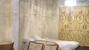 Une petite pièce agréable et chaleureuse, avec un lit, une chaise, un tapis aux couleurs vives et un rideau orné d’un motif de vases.