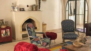 Un salon avec une cheminée, deux fauteuils à motifs, un canapé rouge et un lustre.
