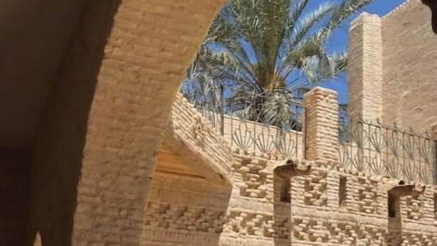Une cour bordée de murs en pierre, avec une porte en bois et de grands pots.