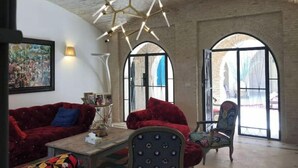 Une pièce spacieuse avec un plafond haut, un lustre moderne, des canapés rouges, un fauteuil à motifs et de grandes fenêtres en arc de cercle.