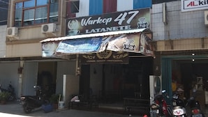 Fachada com um letreiro indicando 'Warkop 47 LATANETE' e um anúncio de cafeteria acima.