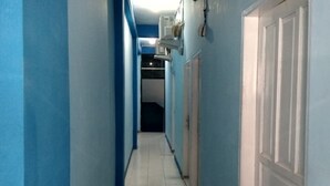 Um corredor estreito com paredes azuis e portas brancas, que leva a um cômodo escuro ao fundo.