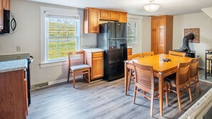 Una cuina amb armaris de fusta, un refrigerador negre, una taula de dinar amb caires i una finestra que dona a una zona verda.