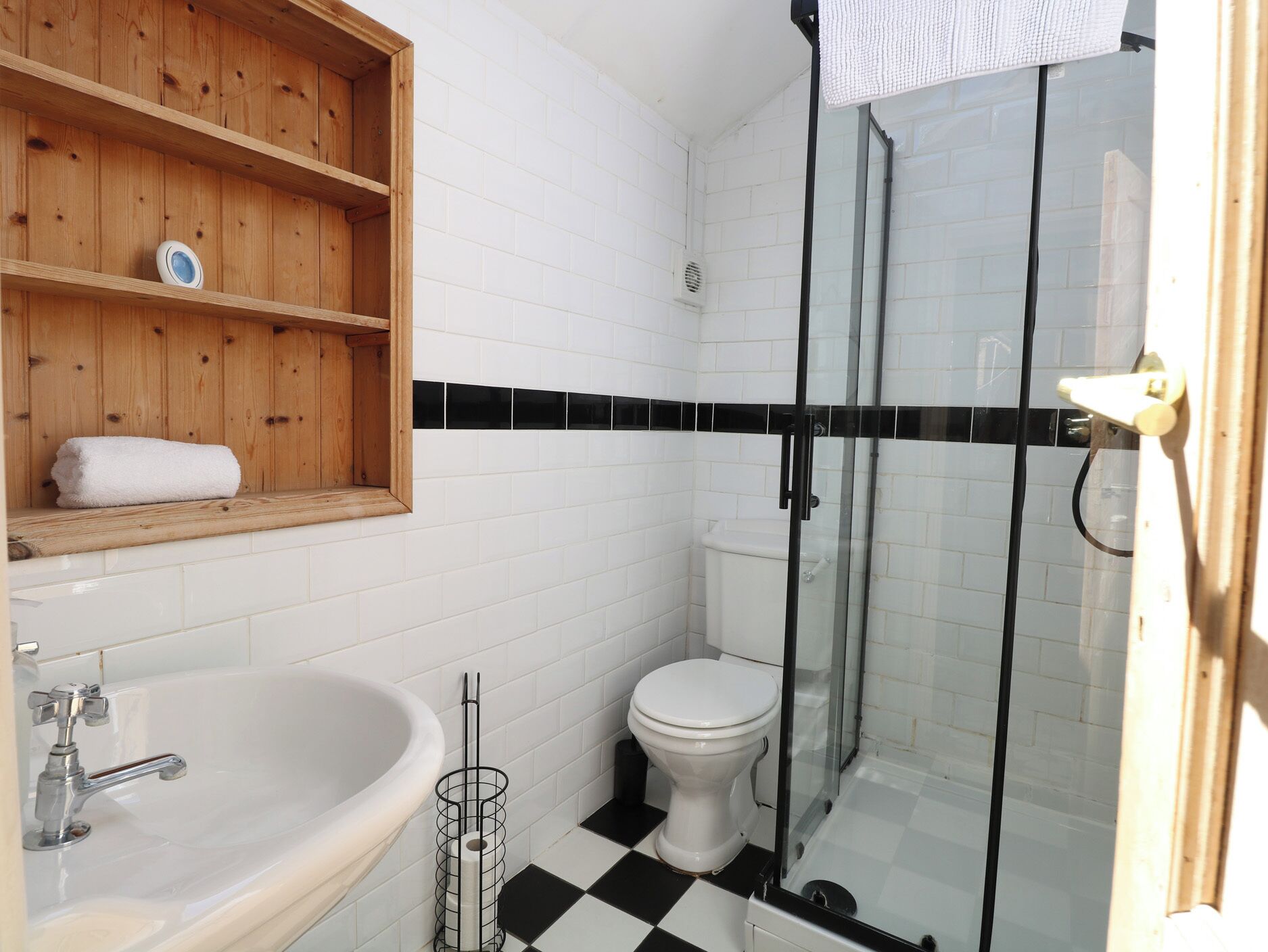 A bathroom with a wooden shelf, a bathtub, a toilet, and a glass shower enclosure.