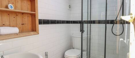 A bathroom with a wooden shelf, a white sink, a toilet, and a glass-enclosed shower.