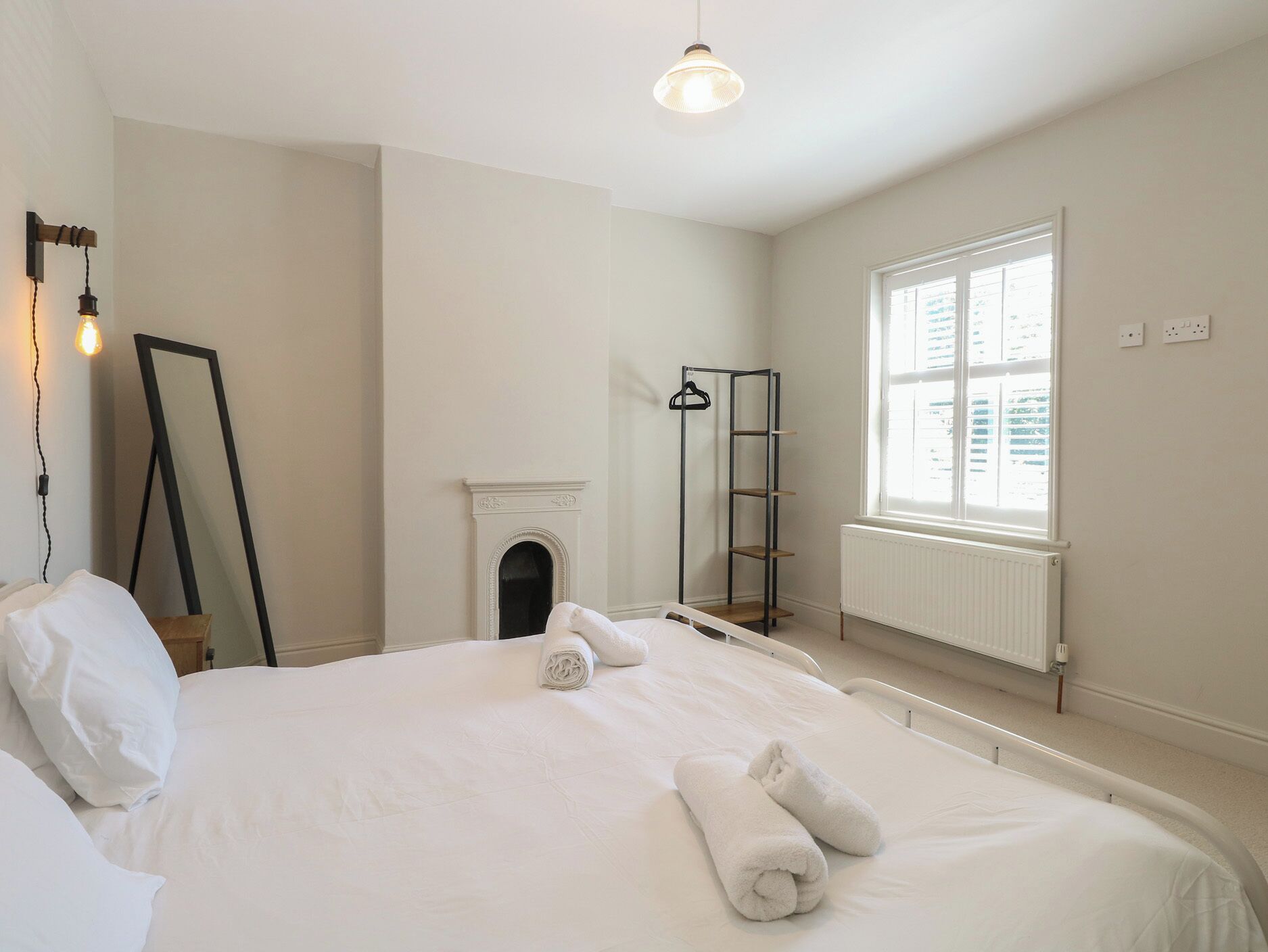 A bedroom with a bed, a mirror, a radiator, and a window.