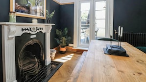 Une pièce avec une cheminée, une table à manger, une vue à travers une porte vitrée et un tableau encadré au mur.