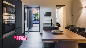 Et moderne køkken med indbygget ovn og mikroovn, et spiseområde med et træbord, og et fjernsyn ophængt på væggen.