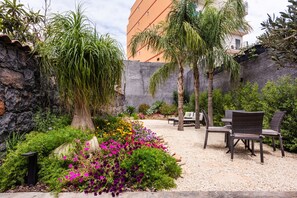 Een tuin met een zithoek, een stenen muur en een gebouw op de achtergrond.