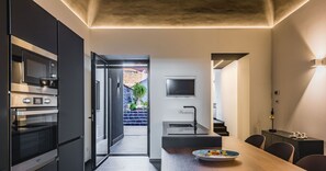 Eine moderne Küche mit Einbauofen und Mikrowelle, ein Essbereich mit Holztisch und ein an der Wand montierter Fernseher.