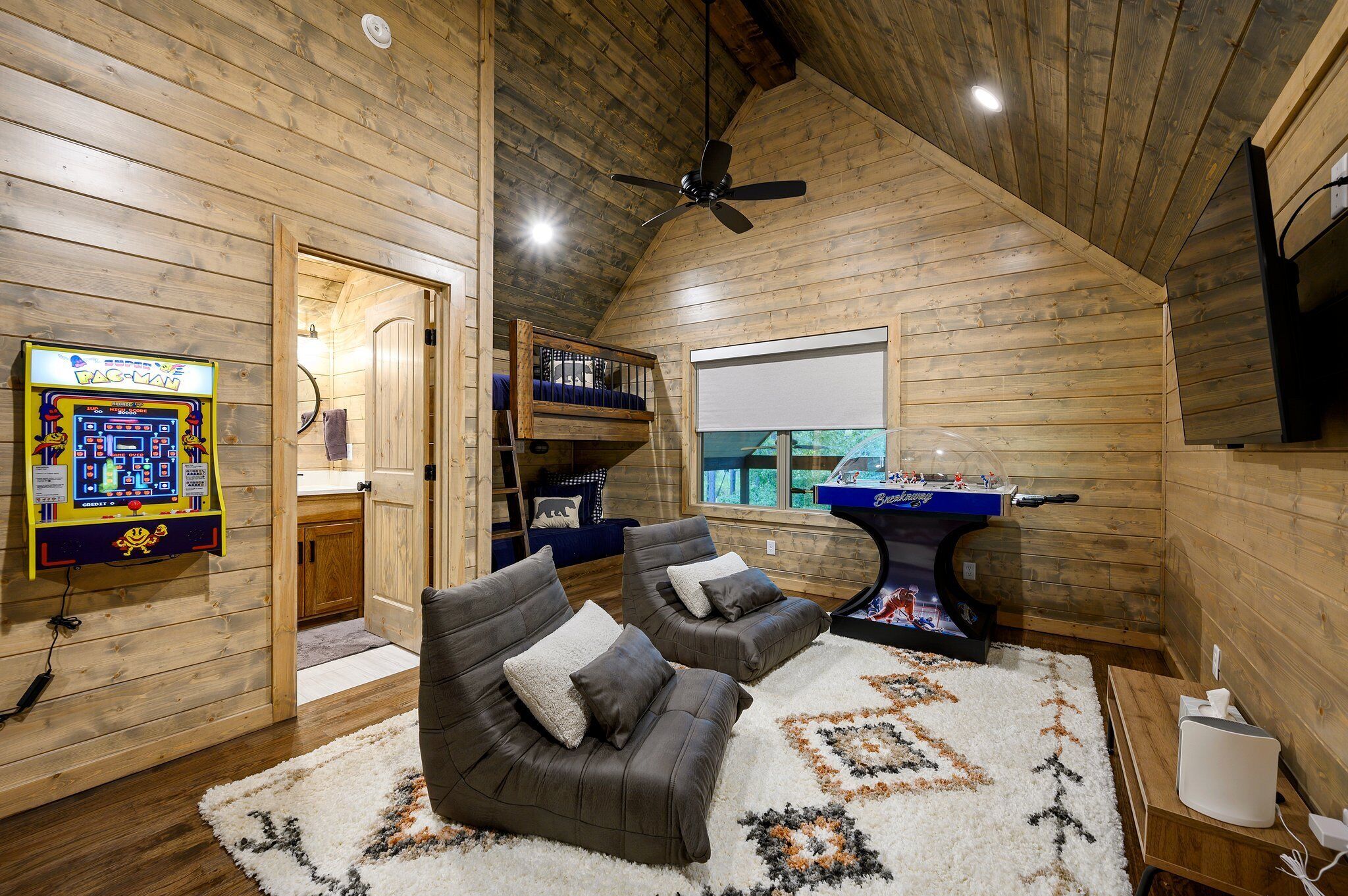 Ein gemütliches Cabin-Interieur mit Holzwänden, Deckenventilator, Billardtisch und zwei Sofas.