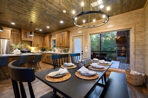 A wooden cabin kitchen with a dining area, a fireplace, and a large window overlooking the outdoors.