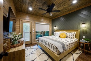 A wooden-paneled bedroom with a bed, a ceiling fan, a TV, and a window with a view.