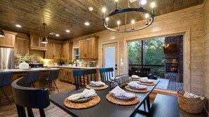 Une cuisine rustique aménagée dans une cabane en bois, avec un coin repas, une cheminée et une grande fenêtre donnant sur l’extérieur.