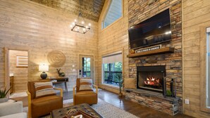 Un salon spacieux avec une cheminée en pierre, des murs en bois et une grande fenêtre.