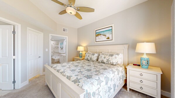 A bedroom with a bed, nightstands, a ceiling fan, a painting, and a door. - New to the Rental Market! (Hilton Head)