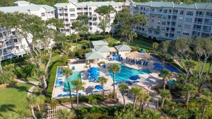 Een resort met meerdere gebouwen, een centraal gelegen zwembadgedeelte met ligbedden en omliggend groen.