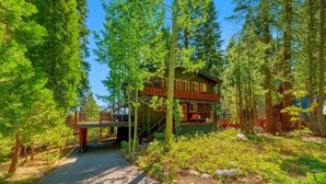 Une cabane dotée d’une terrasse et d’un escalier menant à un deuxième niveau, le tout entouré d’une forêt dense.