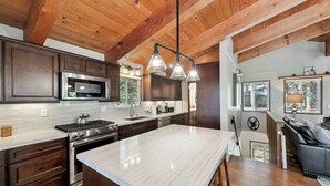 Une cuisine avec des meubles en bois foncé, un grand îlot central, des appareils électroménagers en acier inoxydable et un plafond en bois.
