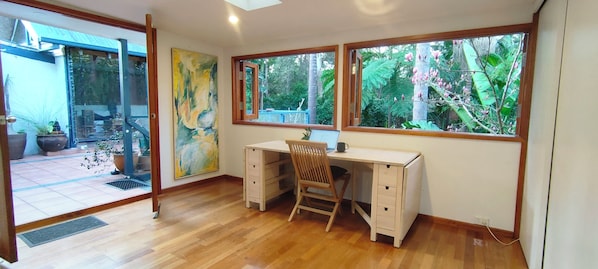 Une pièce dotée d’un bureau et d’une chaise en bois, ainsi que de grandes fenêtres donnant sur un jardin.