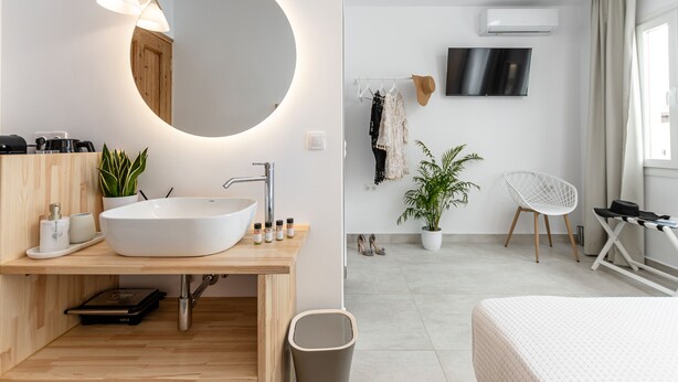 A modern bathroom with a round mirror, white sink, and wooden vanity. - Golden Bird's (Naxos)