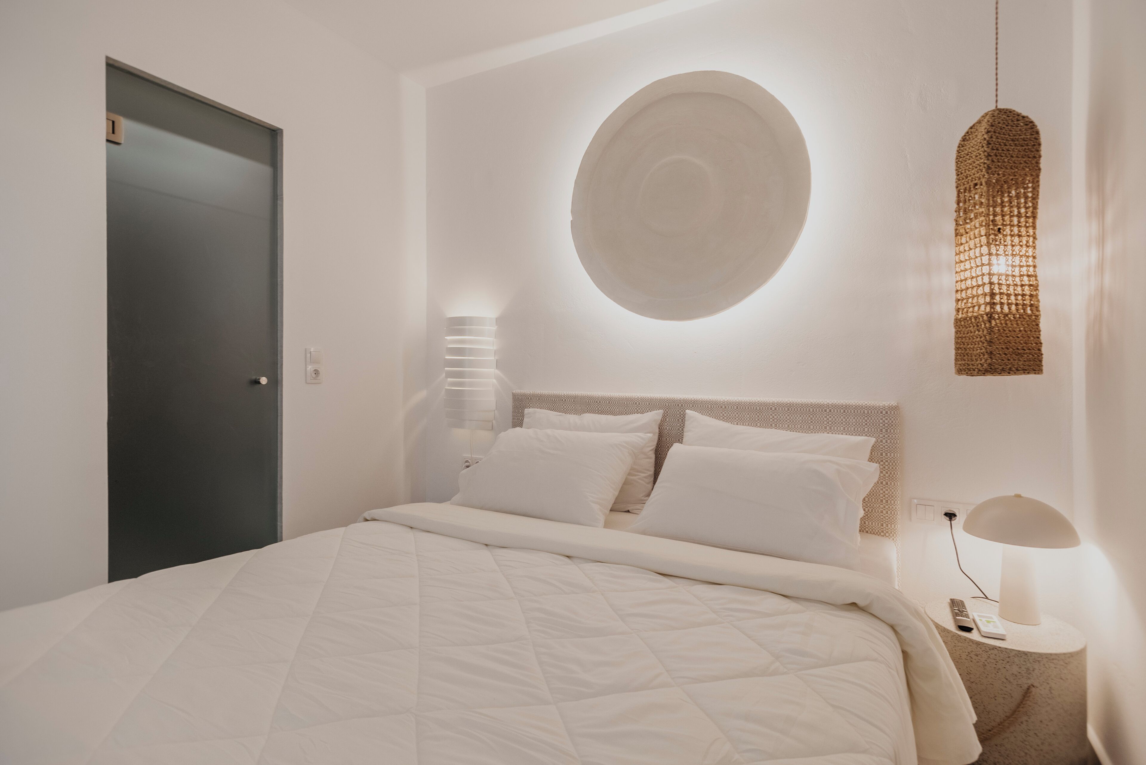 A modern bedroom with a large bed, a round wall decoration, a hanging light fixture, and a bedside table with a lamp.