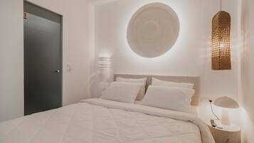 A modern bedroom with a large bed, a round wall decoration, a hanging light fixture, and a bedside table with a lamp.