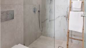 A modern bathroom with a glass-enclosed shower, a toilet, and a wooden towel rack. - Golden Bird's (Naxos)