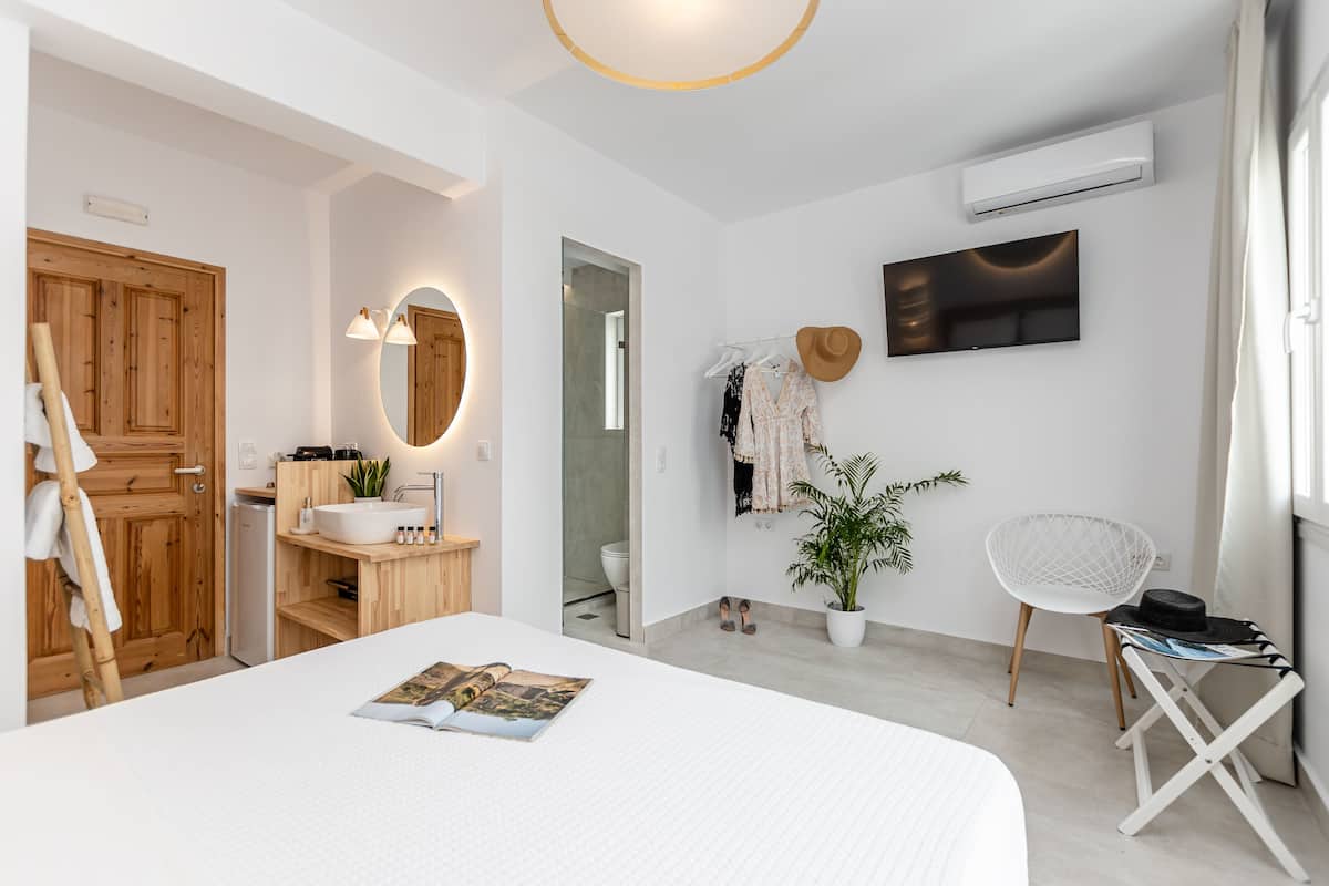 A modern bedroom with a large bed, a wooden wardrobe, a bathroom with a mirror, and a TV on the wall.