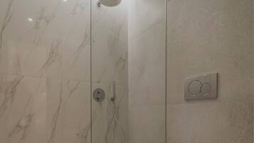 Une salle de bain moderne dotée d’une douche à parois de verre, de toilettes et d’un panneau de commande fixé au mur.