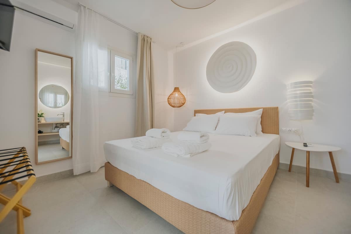 A hotel room with a large bed, a bedside table, a mirror, and a wall-mounted light fixture.
