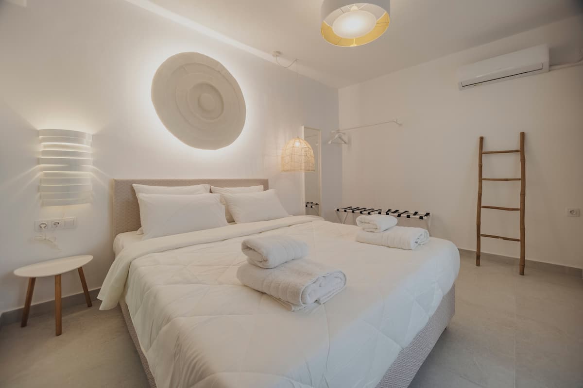 A modern bedroom with a large bed, bedside lamps, a circular wall decoration, and a wooden ladder.