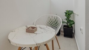 A narrow balcony with a white marble table, a white wire chair, a potted plant, and a hanging light fixture. - Golden Bird's (Naxos)