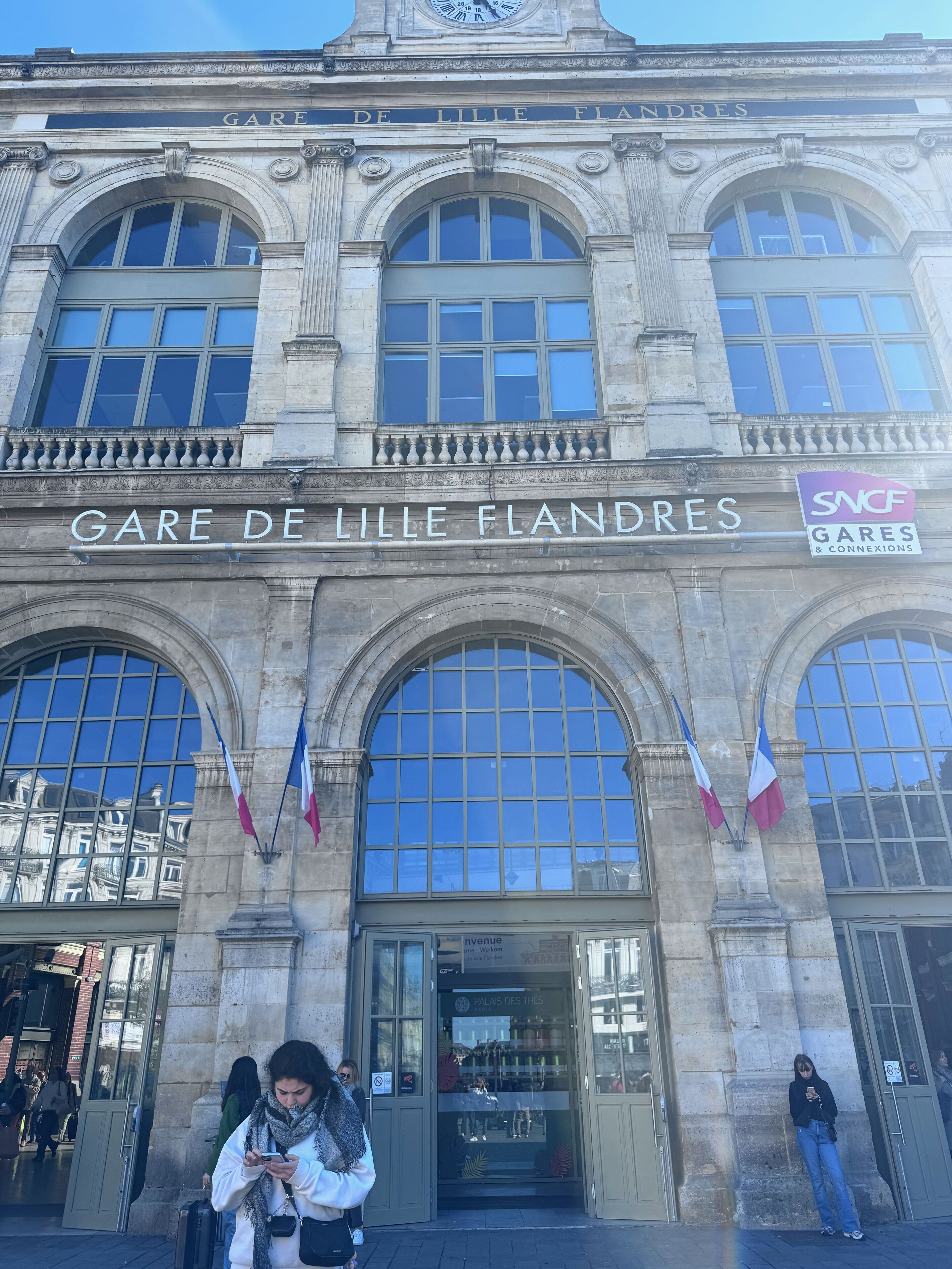 A historic building with the sign "Gare de Lille Flandres" and flags.