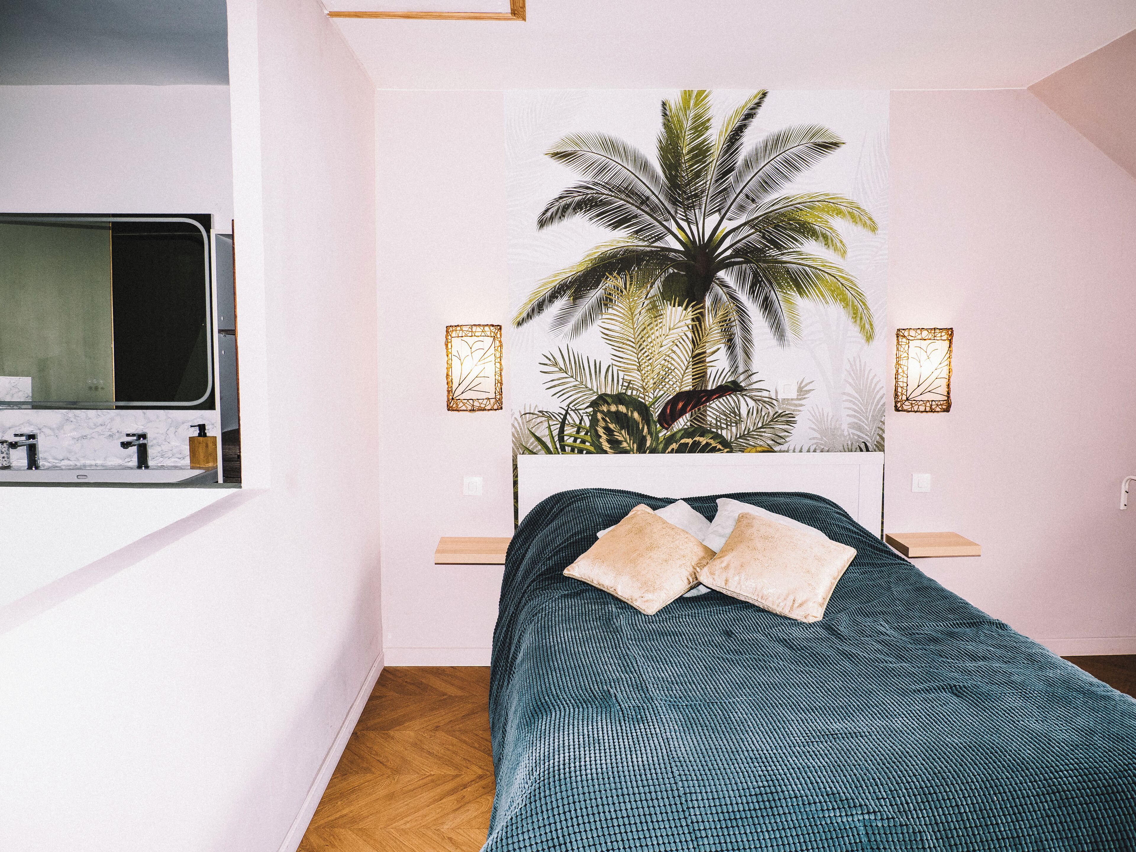 A bedroom with a bed, a nightstand, a mirror, and a wall-mounted light fixture.