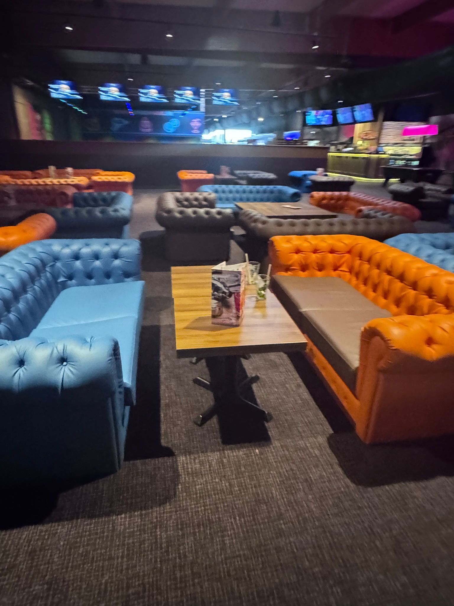 Eine Sitzecke mit mehreren Sofas und einem Tisch, gestaltet in verschiedenen Farben, mit einem zentralen Tisch, auf dem Getränke und eine Speisekarte stehen.