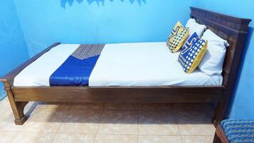Un lit recouvert d’une couvre-lit bleue et blanche, deux oreillers à motifs bleus et jaunes, et une tête de lit en bois.