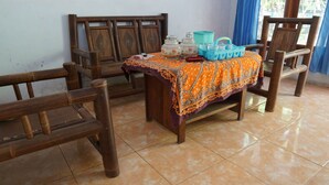 Una habitación con una mesa de madera cubierta por un mantel naranja estampado, dos sillas y un recipiente de plástico azul con asa.