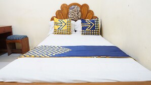 Una cama con cabecera de madera, ropa de cama blanca y almohadas con estampado azul y amarillo.